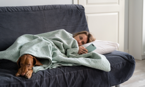 Frau mit Hund liegt krank auf dem Sofa