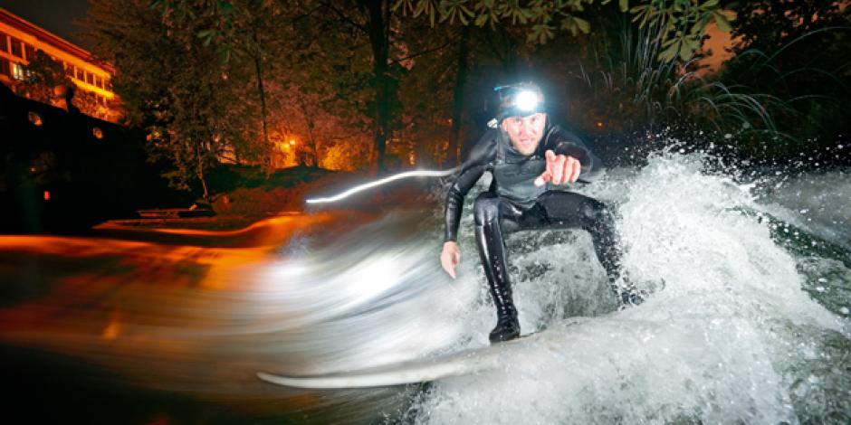 Surfer bei Nacht in der Eisbachwelle in München. 