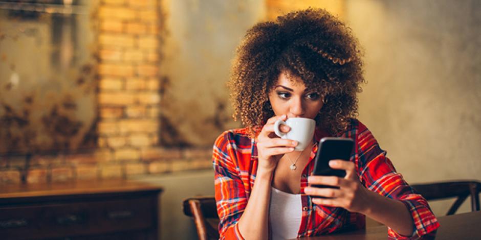 Junge Frau trinkt Kaffee und schaut auf ihr Smartphone