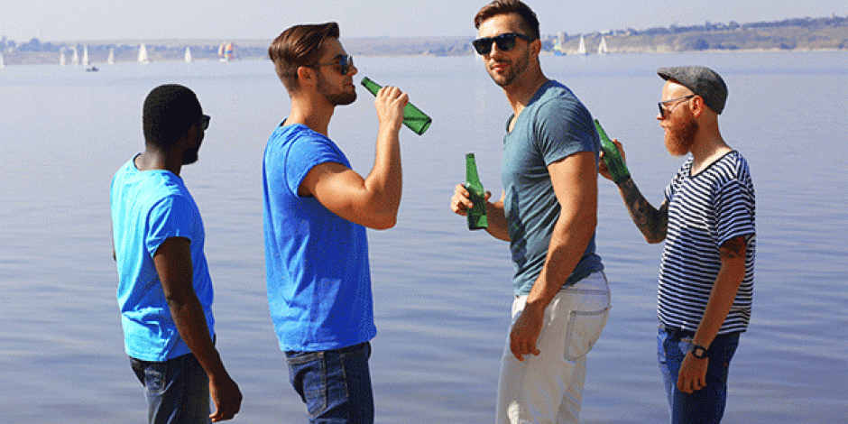 Vier Männer stehen am Rand eines Sees und trinken Bier