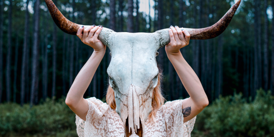 Frau hält Schädel eines Tiers mit Hörnern vor ihr Gesicht