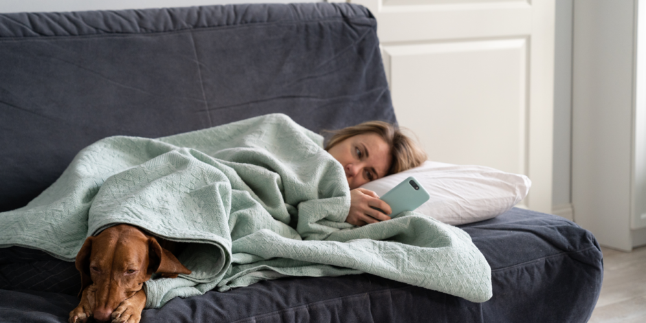 Frau mit Hund liegt krank auf dem Sofa