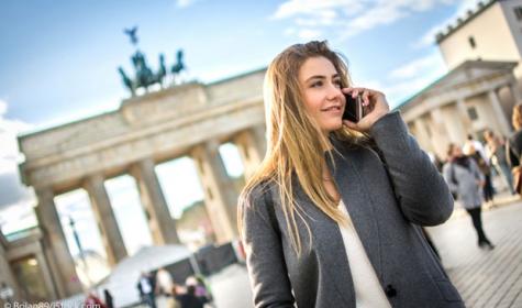 Frau telefoniert mit Brandenburger Tor im Hintergrund