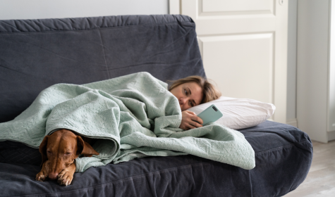 Frau mit Hund liegt krank auf dem Sofa